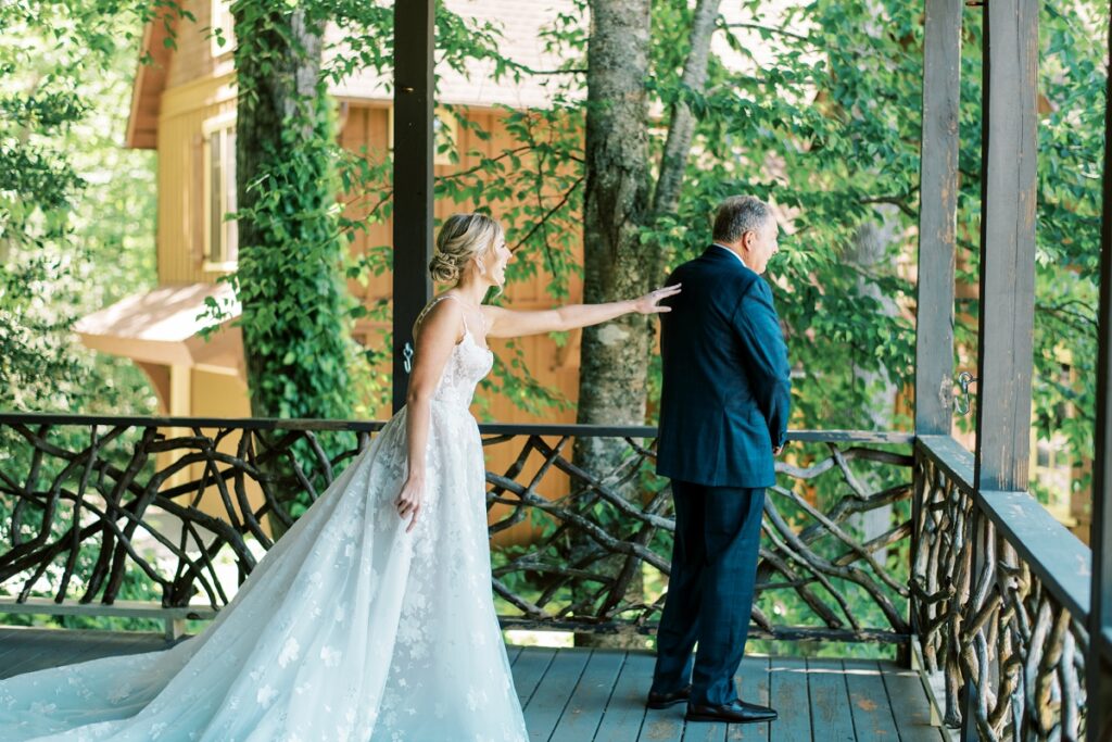 A bride playfully touches her father on a scenic outdoor balcony during a wedding photoshoot amidst lush greenery.