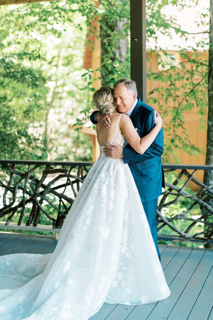 Elegant bride in a lace wedding gown embracing an elderly man outdoors, capturing a heartfelt moment, with lush green trees in the background, photographed by Meghan Rose Photography.