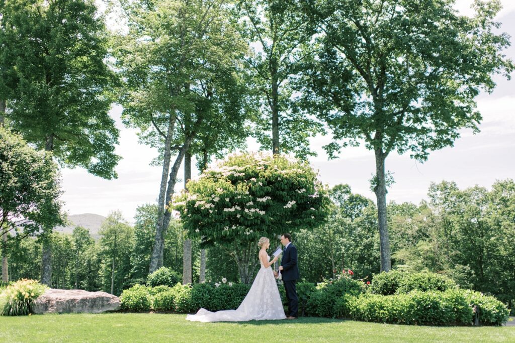 Elegant outdoor wedding ceremony featuring a bride and groom exchanging vows under lush green trees in a scenic garden setting.