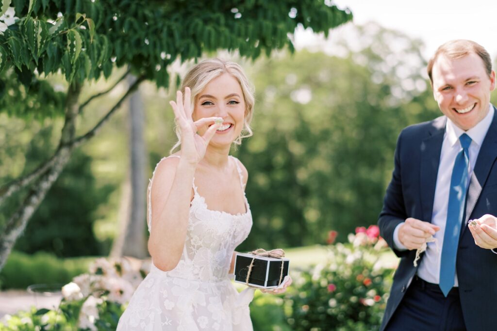 Bright smiling couple at wedding outdoors, woman holding small gift box, wedding photography by Meghan Rose Photography, romantic garden setting, candid moment capturing joy and celebration.