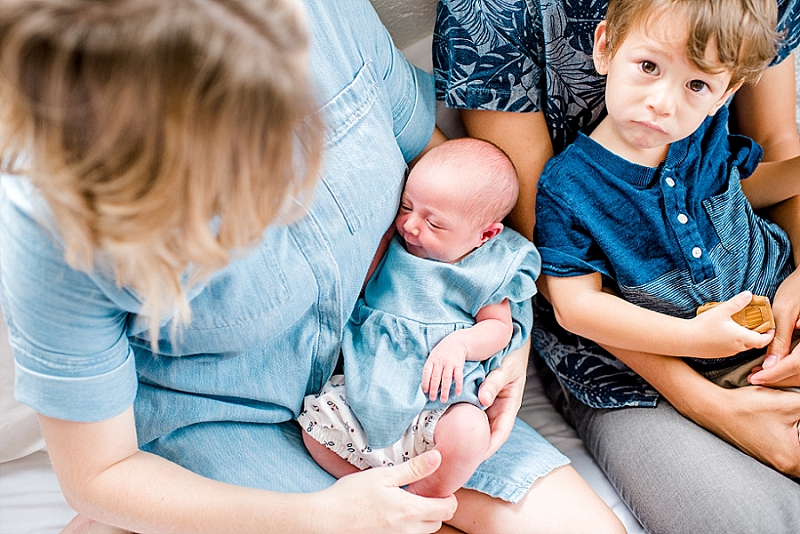 Close-up of a newborn baby resting on a mother's lap with a young boy sitting beside them, family outdoor photography, candid moment.