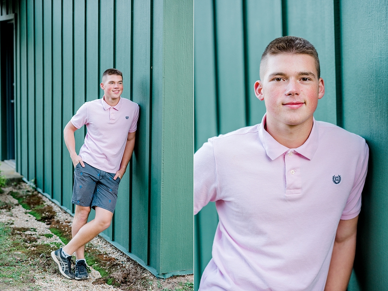 senior boy in pink polo leaning on green barn