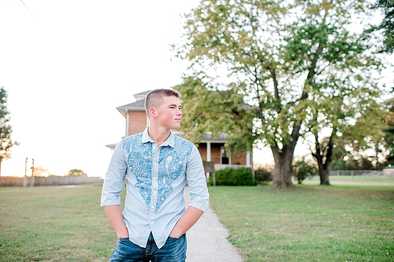 senior photo of boy in blue shirt in front of brick house